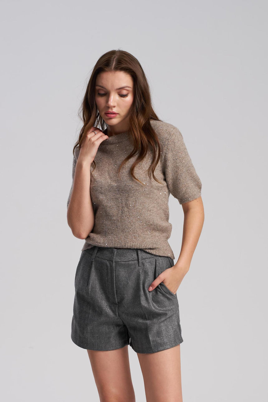 Woman wearing a brown sweater and gray shorts on a light gray background