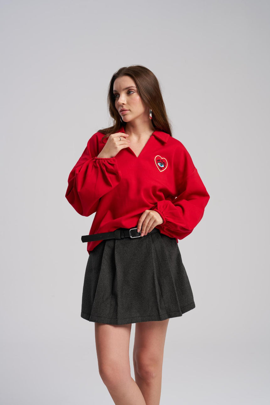 Woman wearing a red blouse with a heart design and a black skirt on a gray background